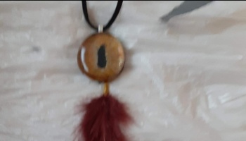 Handmade necklace with an amber eye pendant and a burgundy feather tassel on a black cord.