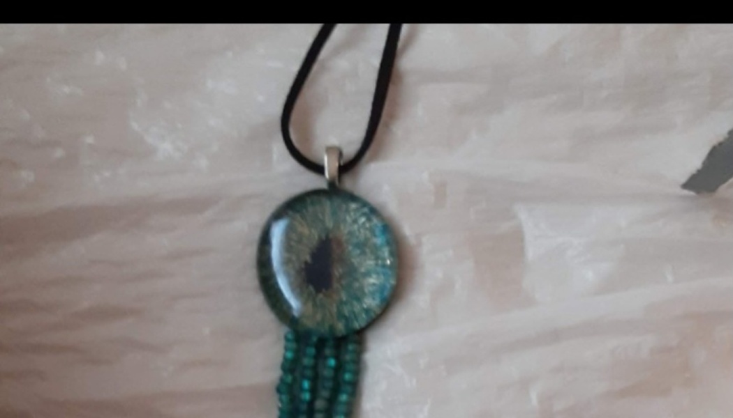 Teal glass dragon eye pendant necklace featuring hanging beaded fringe on a black cord.