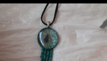 Teal glass dragon eye pendant necklace featuring hanging beaded fringe on a black cord.