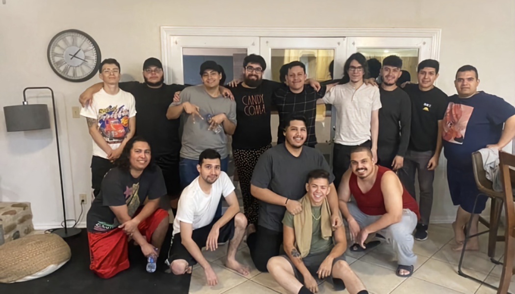 A group of young men standing and crouching together, smiling inside a home.