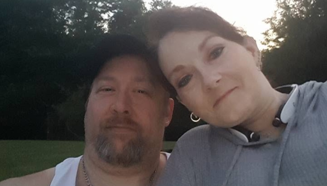 A man with a goatee and a woman leaning her head against him pose for a selfie outdoors at dusk.