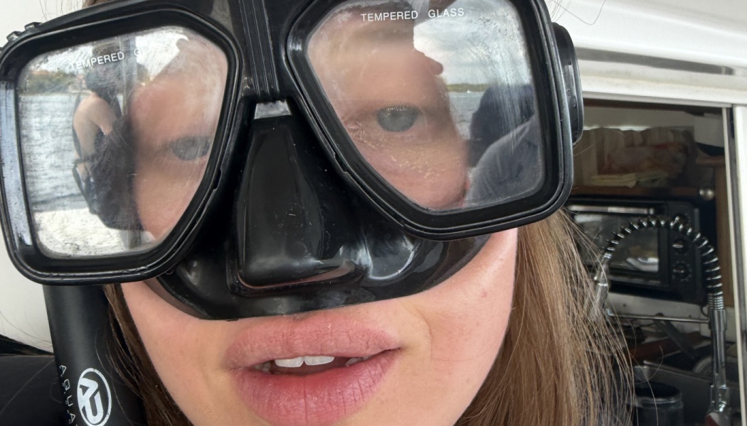 Close-up selfie of a woman wearing a black scuba diving mask on a boat.