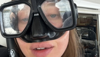 Close-up selfie of a woman wearing a black scuba diving mask on a boat.