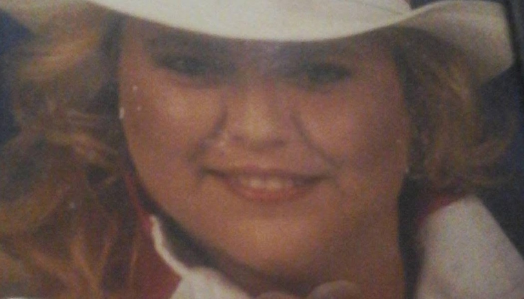 Close-up portrait of a smiling woman with blonde hair wearing a white cowboy hat.