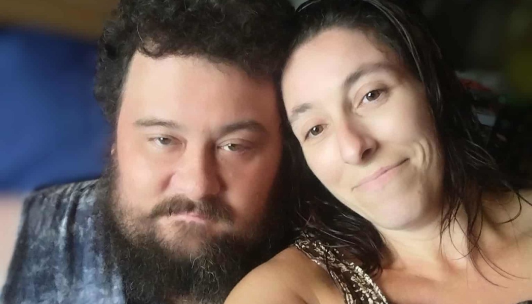 Close-up portrait of a bearded man with dark curly hair and a smiling woman leaning close together.