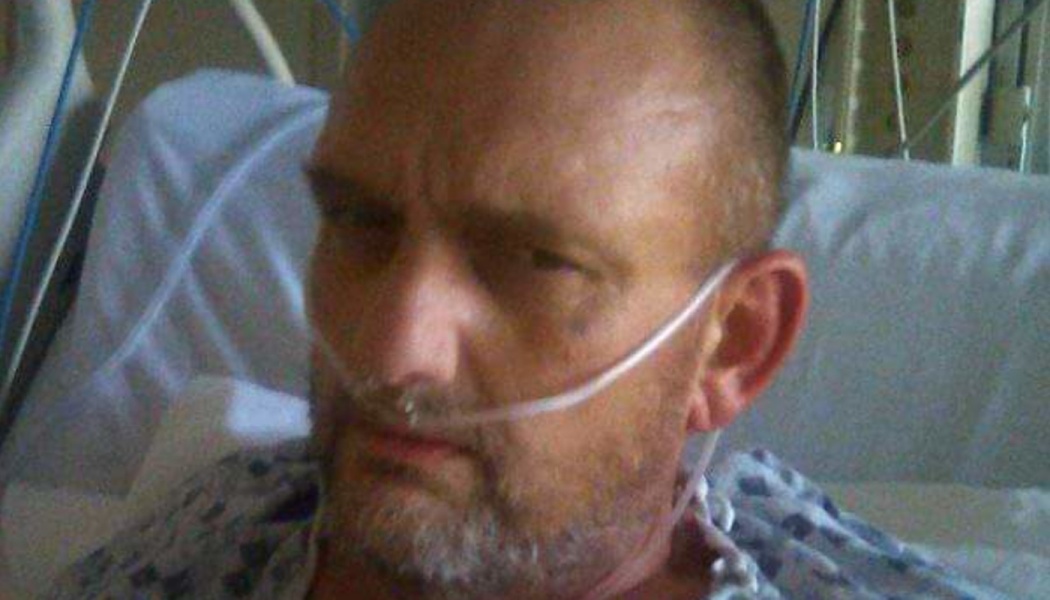 A man lying in a hospital bed wearing a gown and a nasal oxygen cannula.