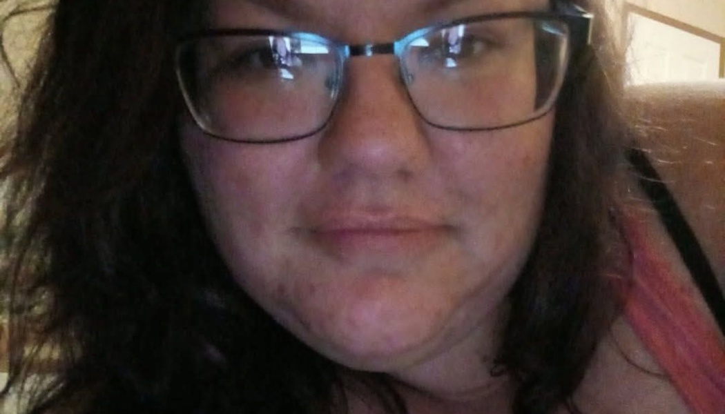 Close-up selfie of a woman with dark wavy hair wearing black-framed glasses.
