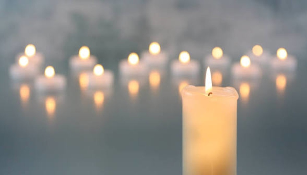 A glowing pillar candle stands in the foreground with softly blurred tea lights lit in the background.
