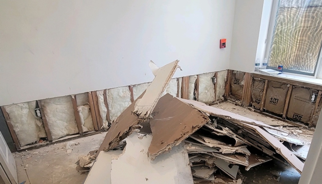 Broken drywall debris piled in a room with exposed wall studs and fiberglass insulation.