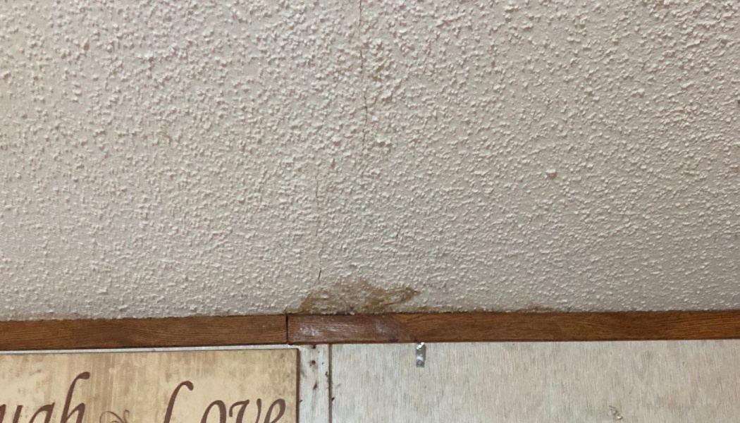 Popcorn ceiling with a vertical crack and brown water damage stain above wood wall trim.