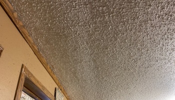 Textured popcorn ceiling meeting a beige interior wall trimmed with dark wood.