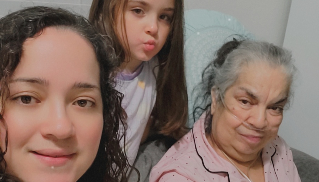Three generations of a family pose for a selfie, including an elderly woman wearing a nasal cannula.
