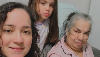 Three generations of a family pose for a selfie, including an elderly woman wearing a nasal cannula.