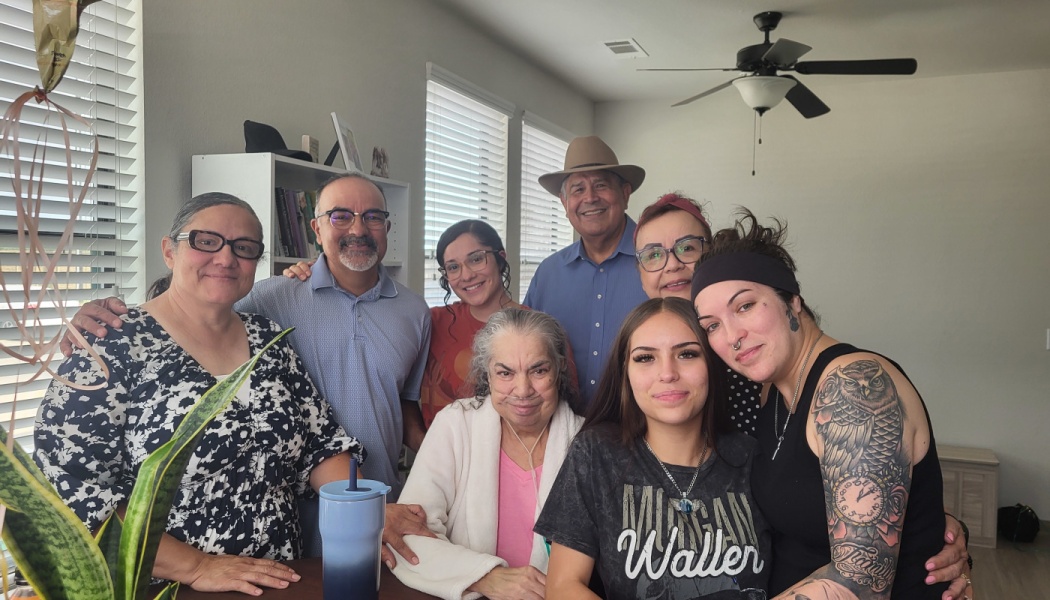 A smiling multi-generational family poses closely around an elderly woman wearing nasal oxygen tubing.