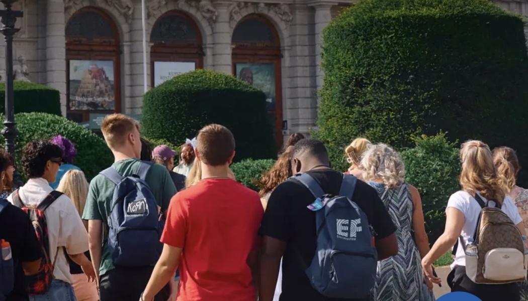 Group of young students with backpacks walking toward a grand historic museum.
