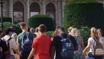 Group of young students with backpacks walking toward a grand historic museum.