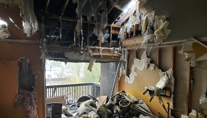 Severely fire-damaged room with torn walls, exposed wooden studs, melted insulation, and charred ceiling joists.
