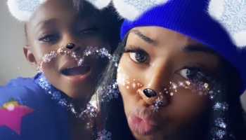 A woman in a blue beanie and a child pose together with a winter snowflake photo filter.