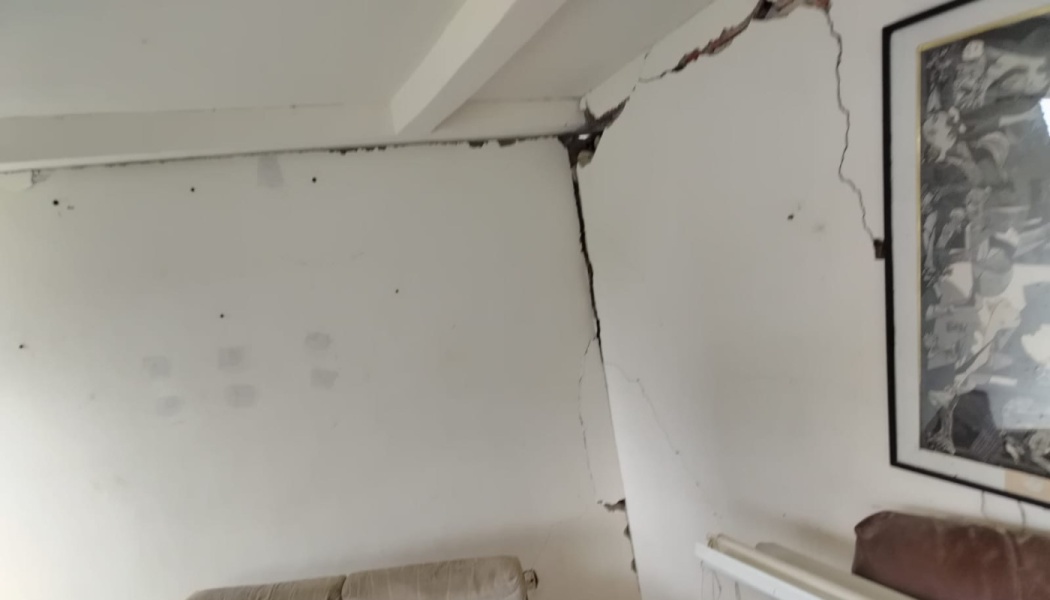 Severe structural cracks splitting white interior walls near the ceiling inside a home.