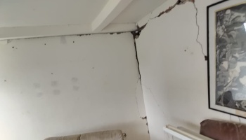 Severe structural cracks splitting white interior walls near the ceiling inside a home.