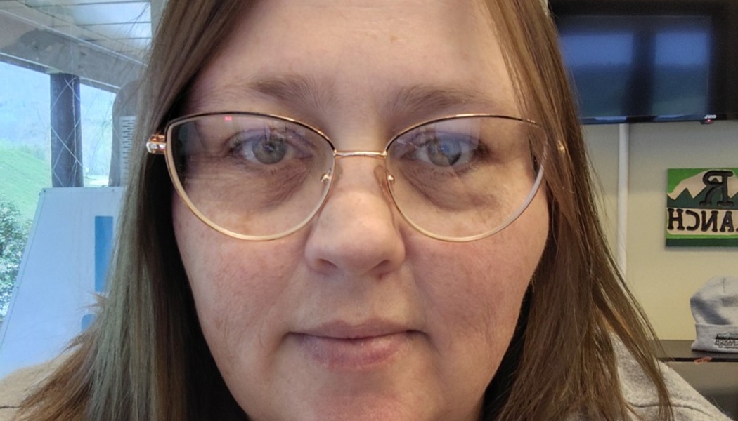 Close-up portrait of a woman with light brown hair wearing wire-frame cat-eye glasses, looking at the camera.