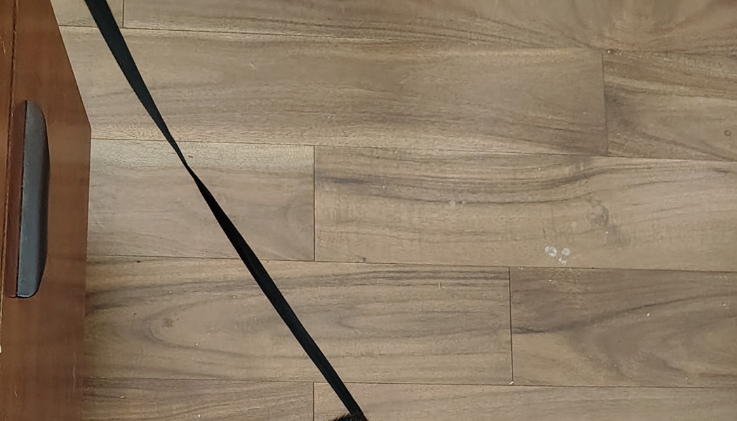Black strap extending across light wood plank flooring next to a wooden cabinet.