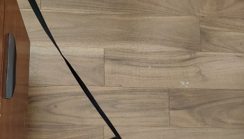 Black strap extending across light wood plank flooring next to a wooden cabinet.
