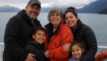 A smiling multi-generational family of five poses together outdoors on a boat in front of misty mountains.