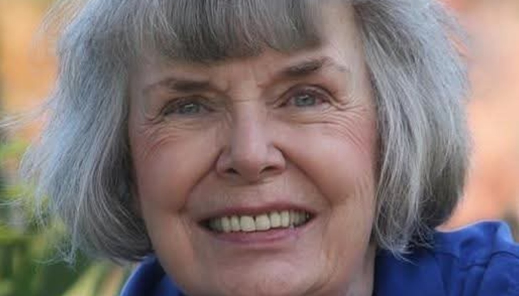Smiling senior woman with short gray hair and blue eyes, wearing a blue shirt.