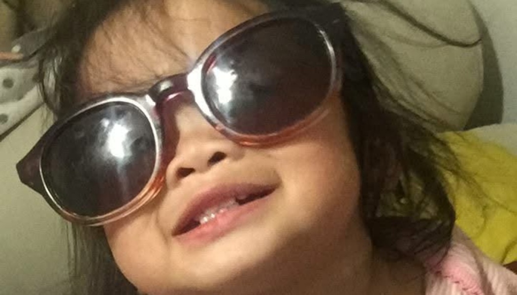 Close-up of a smiling toddler wearing oversized dark sunglasses.