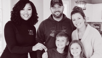 A housing representative hands new keys to a smiling family of four inside their home.