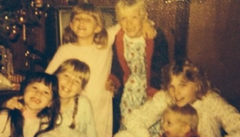A grainy vintage snapshot of smiling children and family members gathered together in cozy pajamas.