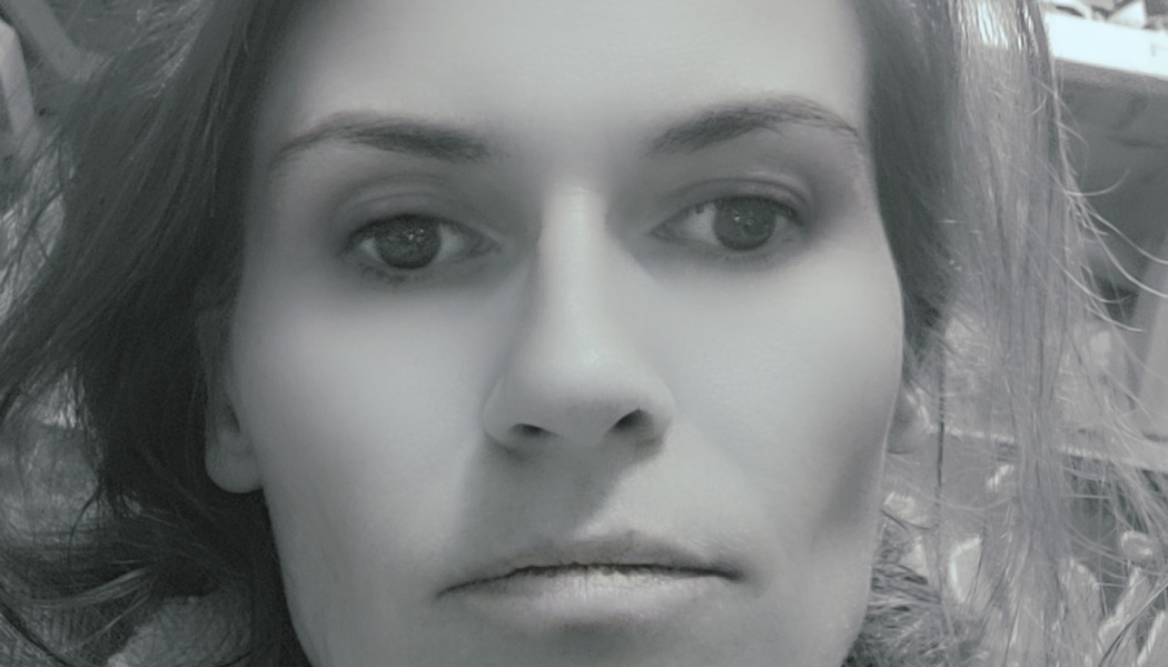 Black and white close-up portrait of a woman looking directly at the camera with a serious expression.