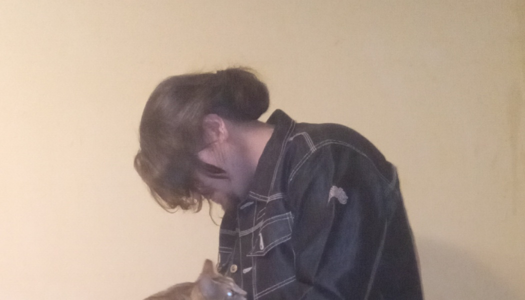 Side profile of a person with hair in a bun wearing a dark denim jacket, looking down at a small pet.