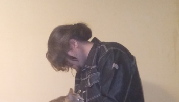 Side profile of a person with hair in a bun wearing a dark denim jacket, looking down at a small pet.