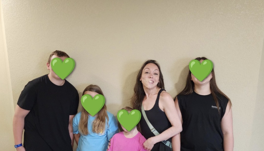 A smiling woman poses with four children whose faces are covered with green heart emojis.