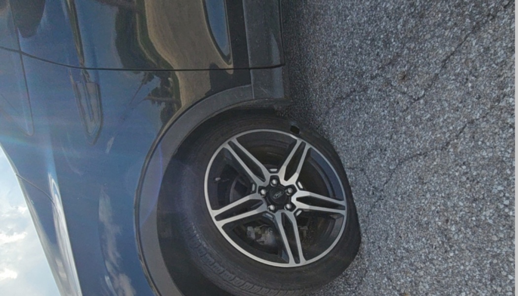 Close-up of a damaged tire with a tear in the sidewall on a dark Ford car parked on asphalt.