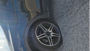 Close-up of a damaged tire with a tear in the sidewall on a dark Ford car parked on asphalt.