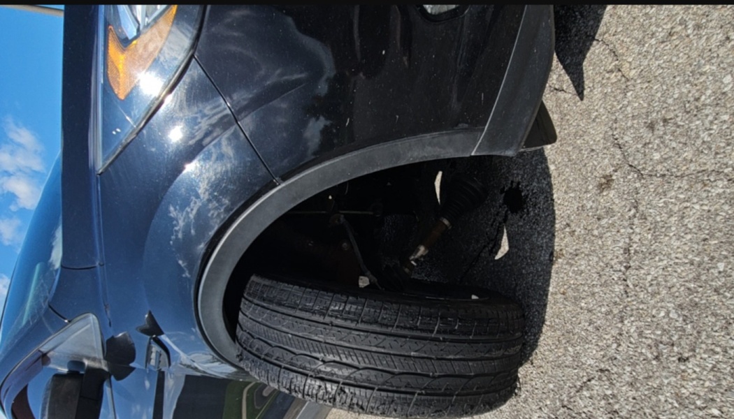 A black car with a severely damaged front axle and tire detached inside the wheel well.