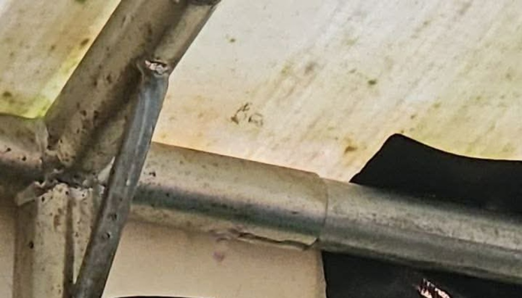 Close-up of a rusted metal frame supporting a dirty, worn white canopy cover.