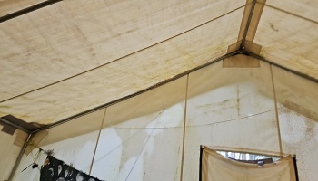 Interior of a worn, water-stained canvas tent showing its metal frame poles and roof structure.