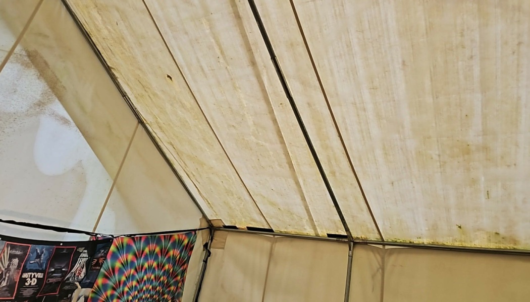 Interior view of a dirty, stained canvas tent ceiling supported by metal frame poles.