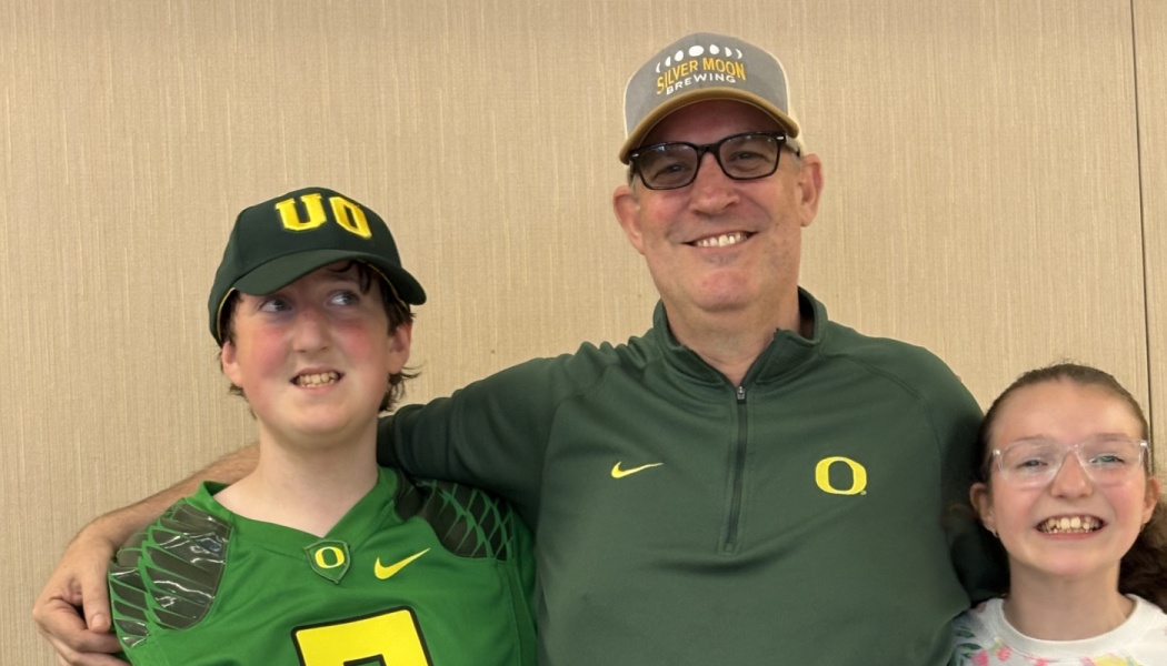 A smiling man poses with his arms around a boy and girl wearing green Oregon Ducks gear.