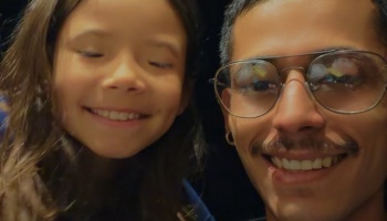 A smiling young man with glasses and a mustache posing close-up with a happy young girl.