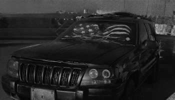 A dark SUV with an American flag sunshade behind its front windshield.