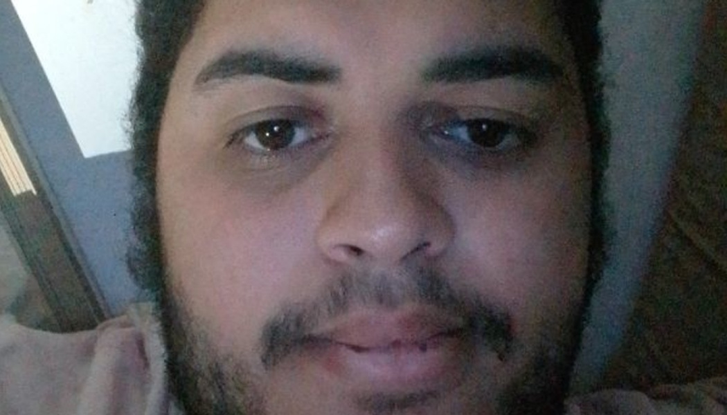 Close-up selfie of a young man with dark hair, a beard, and mustache looking directly at the camera.