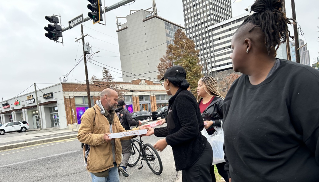 Volunteers hand a pizza box to a man on a city street corner.