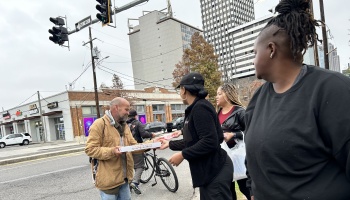 Volunteers hand a pizza box to a man on a city street corner.