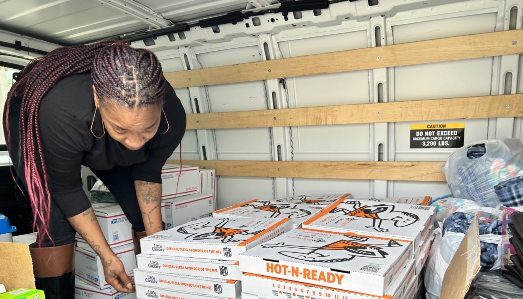 A woman stacks Little Caesars pizza boxes and delivery packages inside a cargo van.
