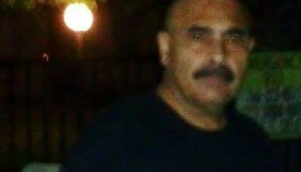 Close-up portrait of a man with a dark mustache wearing a dark t-shirt outdoors at night.